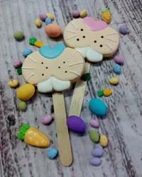 Adorable Hello Kitty style bunny face iced cookie pops on sticks with pastel Easter eggs and carrots